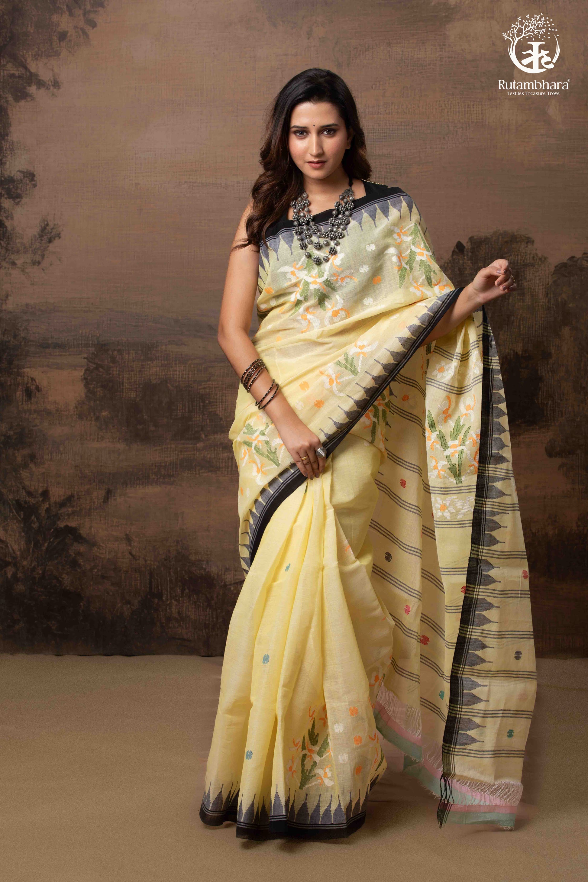 Woman wearing a light yellow saree with a dark border against a brown background