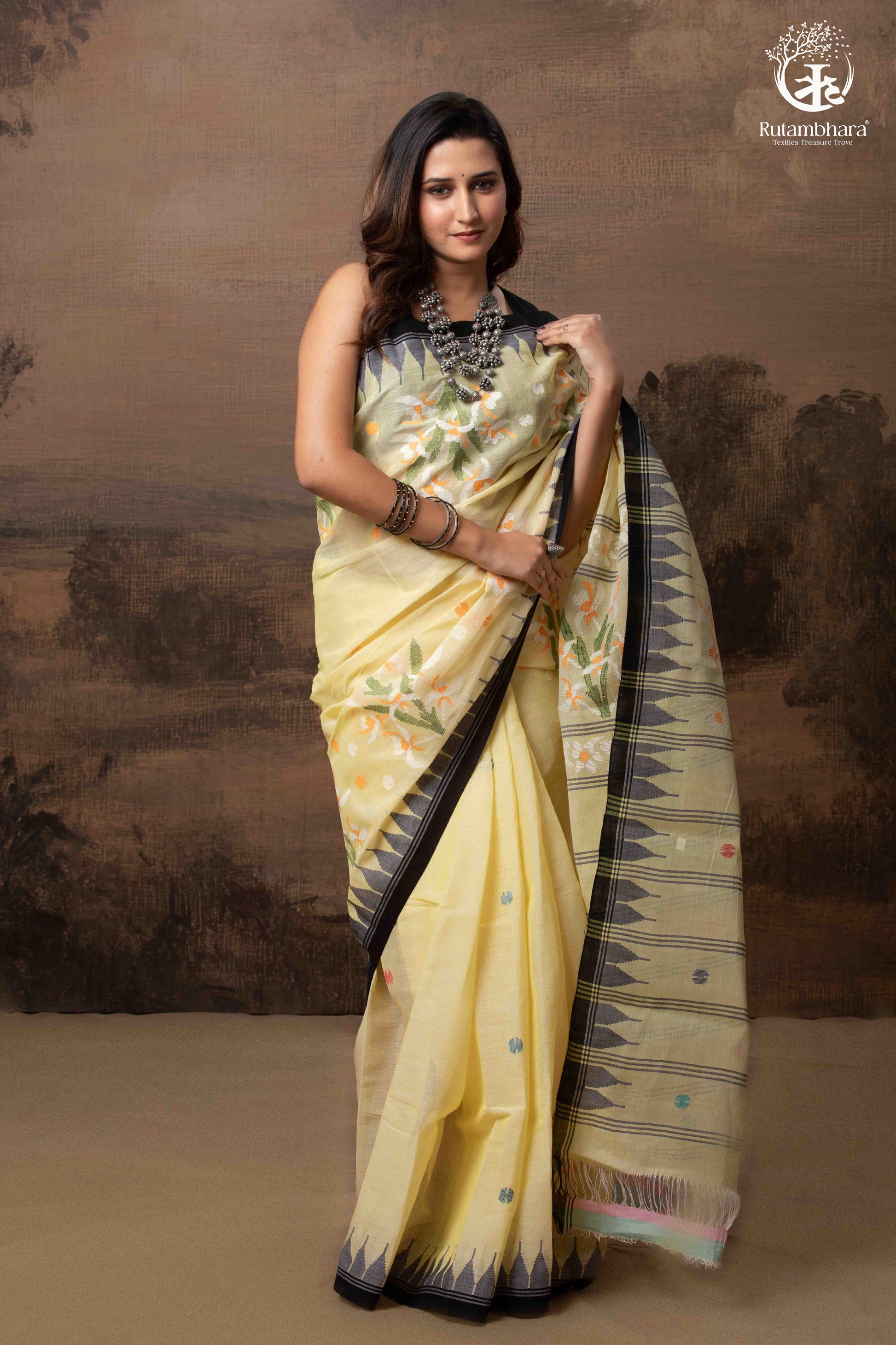 Woman wearing a yellow saree with a black border against a brown background