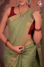 Woman wearing a green saree with a red blouse, posing against a neutral background.