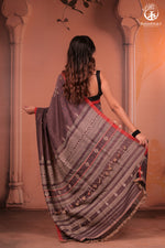 Woman holding a patterned saree in front of an architectural background