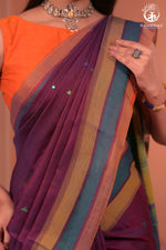 Person wearing an orange blouse with a purple saree featuring colorful stripes.
