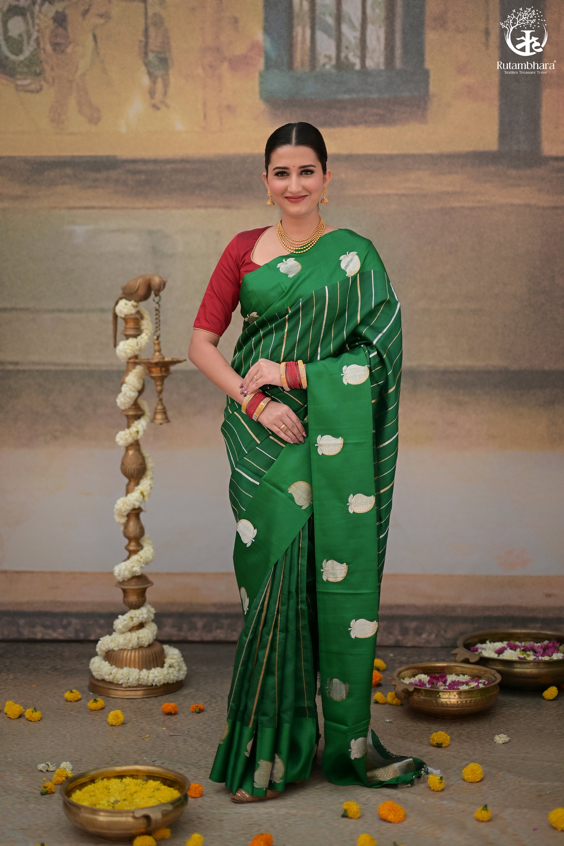 A woman modeling a royal green Banarasi saree with sona-rupa zari kairi motifs in a traditional setting, with decorative items and offerings on the floor.