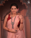 Woman in a traditional pink saree with a red blouse, wearing jewelry, against a decorative background.
