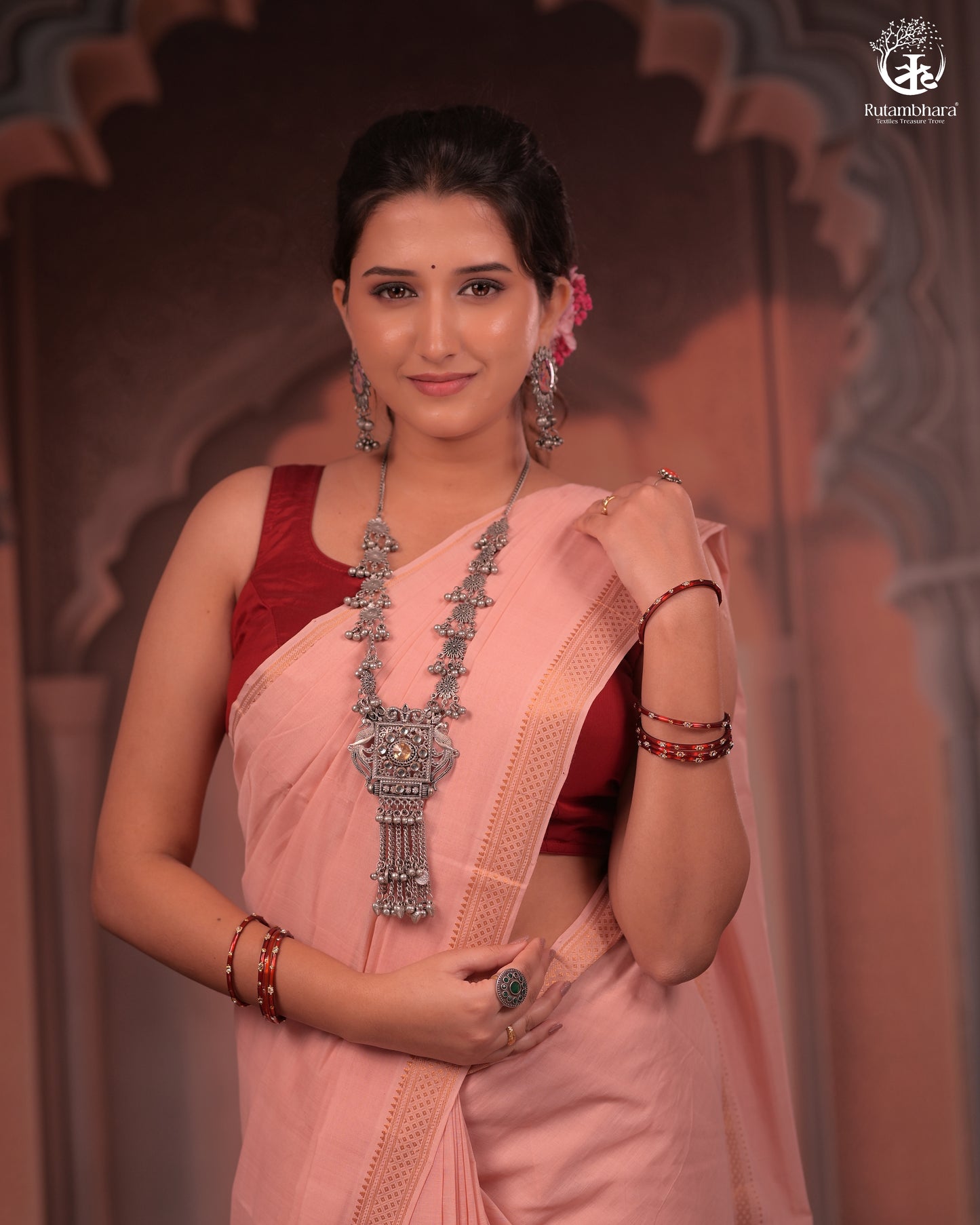 Woman in a traditional pink saree with a red blouse, wearing jewelry, against a decorative background.